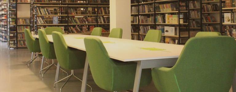 Een tafel met groene stoelen in een bibliotheek